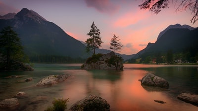 落日时近山被水体包围的岩层上树木的景观摄影